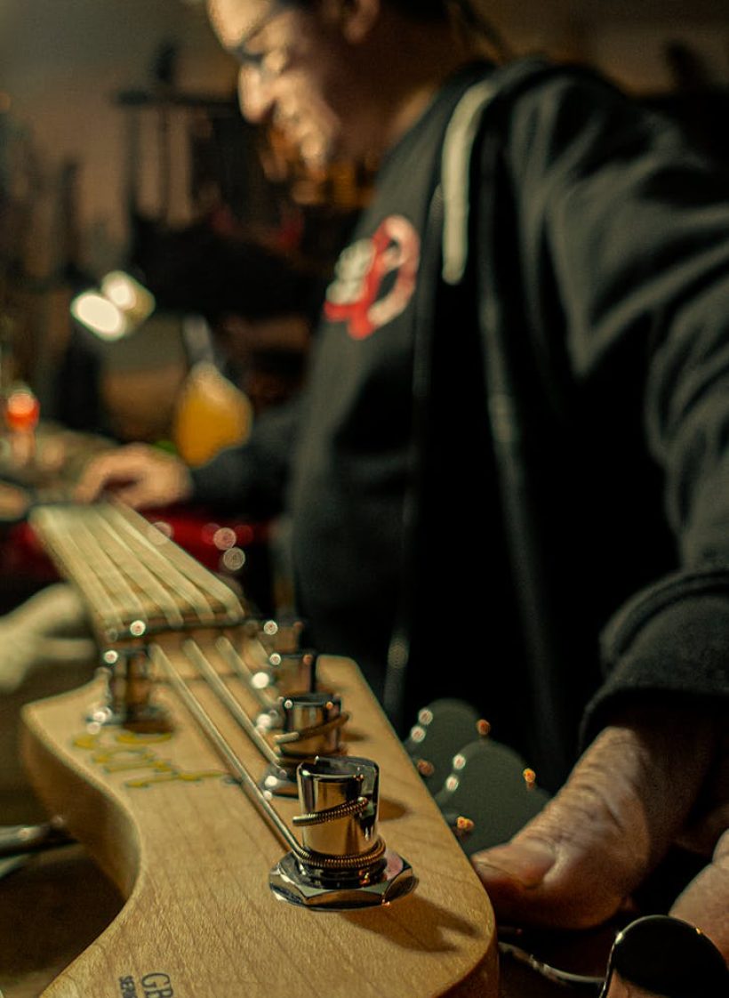 Blurred musician with focus on electric guitar tuning pegs in a workshop setting.